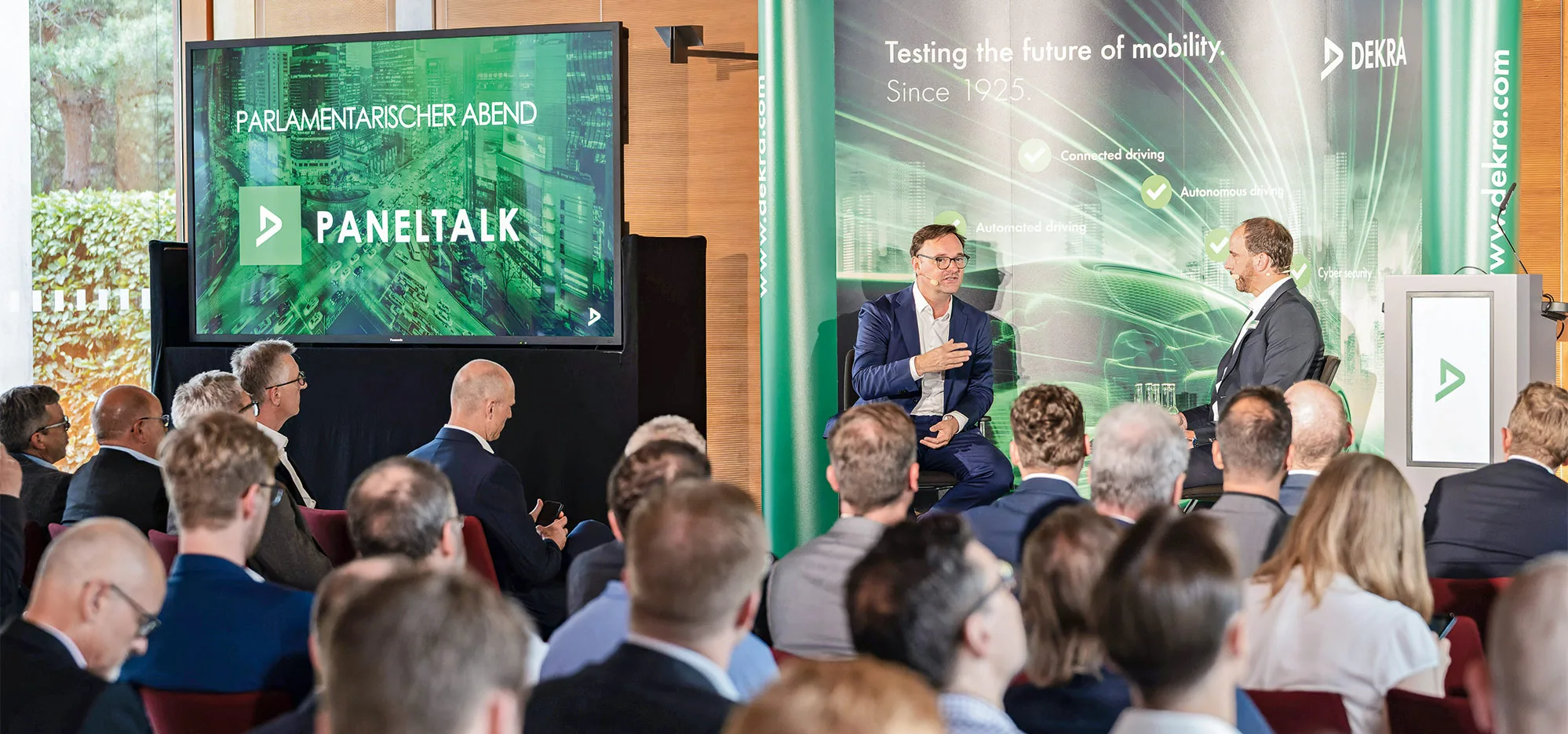 Two people talking in front of an audience at a DEKRA event.