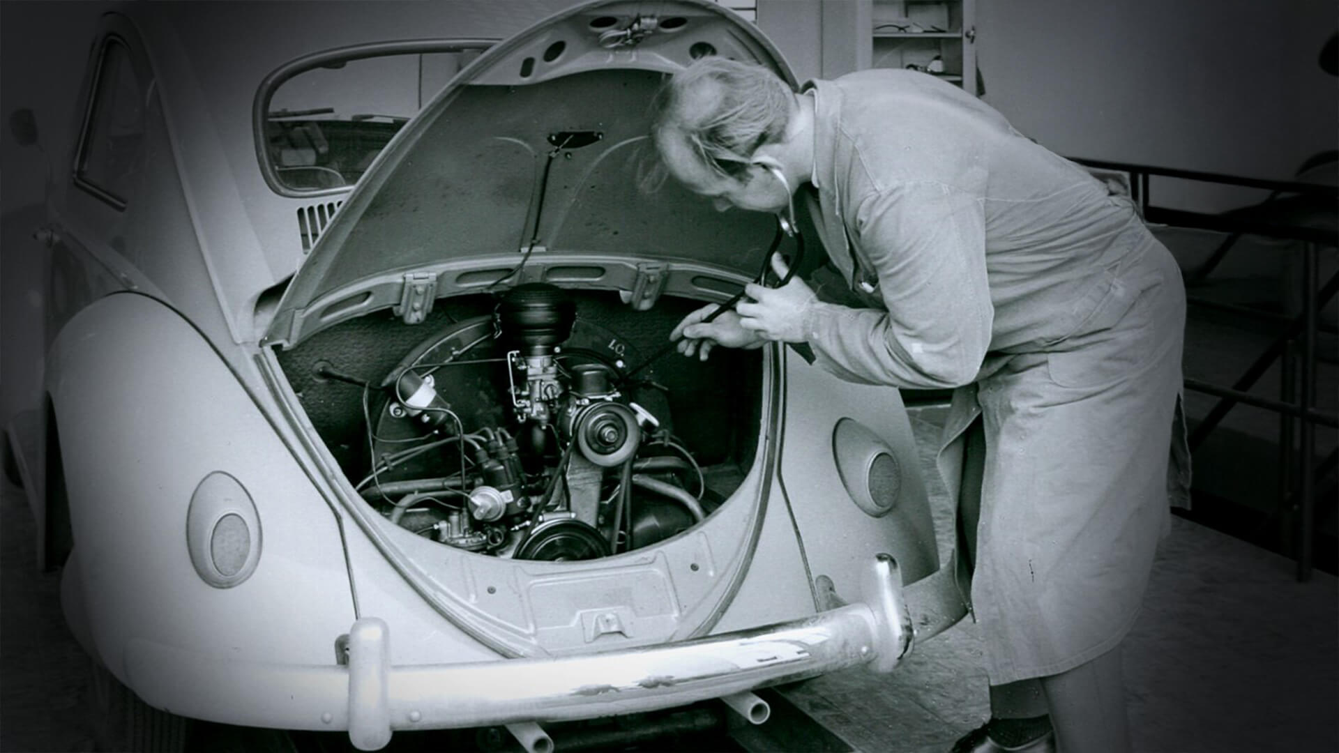 Historische Fahrzeugprüfung eines VW Käfers durch einen Mechaniker.